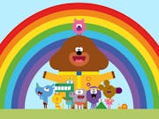 Colourful animation of a large brown dog in scout's leader uniform, surrounded by various small smiling animals in front of a rainbow