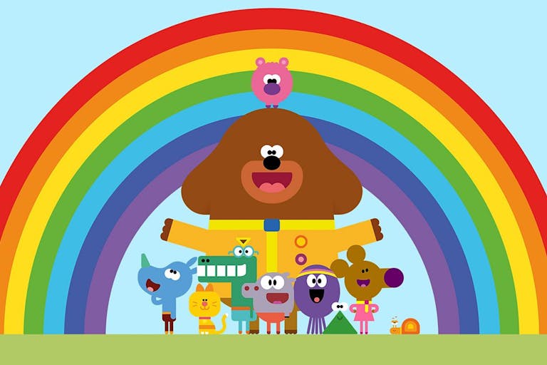 Colourful animation of a large brown dog in scout's leader uniform, surrounded by various small smiling animals in front of a rainbow