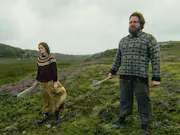 A man and woman standing on a grassy hill, looking threatening as they look ahead holding a weapon in one hand