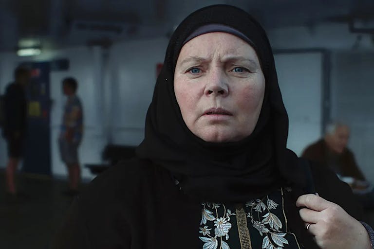 Middle-aged woman wears a black hijab and looks out into the distance.