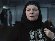 Middle-aged woman wears a black hijab and looks out into the distance.