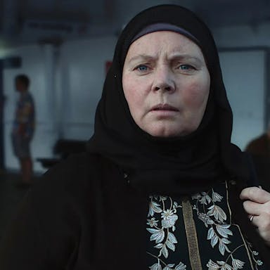 Middle-aged woman wears a black hijab and looks out into the distance.