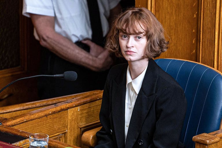 A young white woman with short brown hair sitting in court being questioned