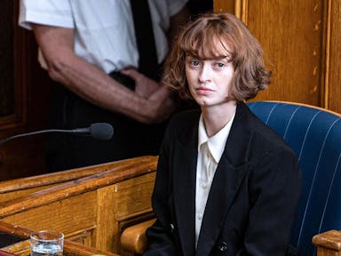 A young white woman with short brown hair sitting in court being questioned