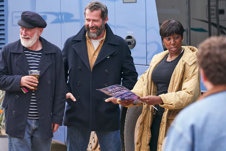 Two men and one woman stand talking and laughing