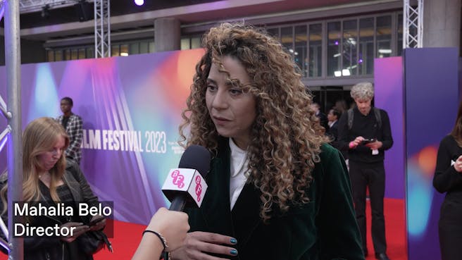 A woman with long curly light and dark brown hair speaking into a mic
