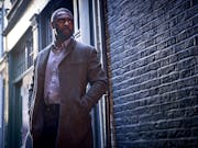 Man with hands in his pockets stands against a brick wall