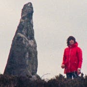 Woman in red raincoat in the distance stands beside a strange shaped large rock
