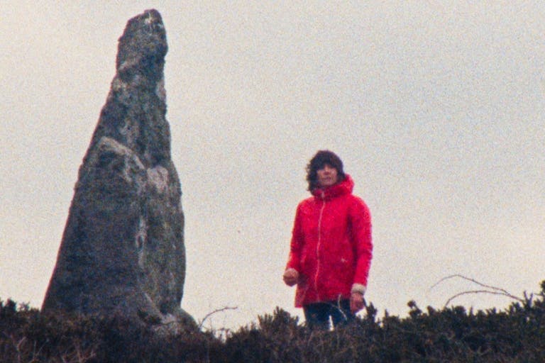 Woman in red raincoat in the distance stands beside a strange shaped large rock