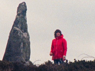 Woman in red raincoat in the distance stands beside a strange shaped large rock