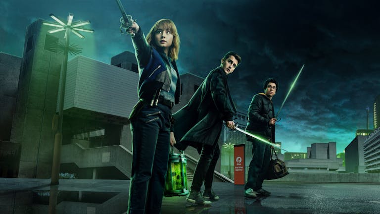Three young adults stand against an industrial night, green-tinged sky, holding swords. 