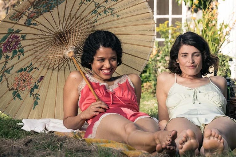 Two glamourous young woman lie on the grass wearing 1940s style nighties, one of them holds a Chinese parasol 