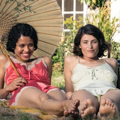 Two glamourous young woman lie on the grass wearing 1940s style nighties, one of them holds a Chinese parasol 