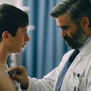 A middle aged white man in a white doctors coat applying wires and monitors to bare torso of a young white man