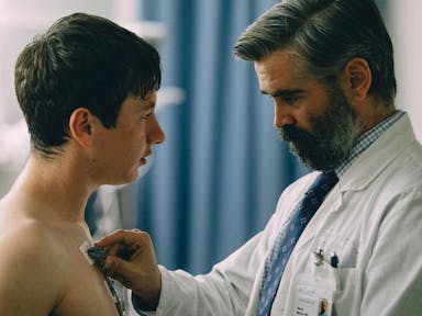 A middle aged white man in a white doctors coat applying wires and monitors to bare torso of a young white man