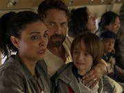 A man, woman and child, hold eachother on a plane, looking very scared.