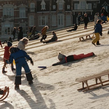 Young children playing on a snowy slope in snow suits and using wooden sledges