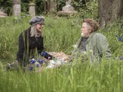 An older man and woman sit in a grassy meadow