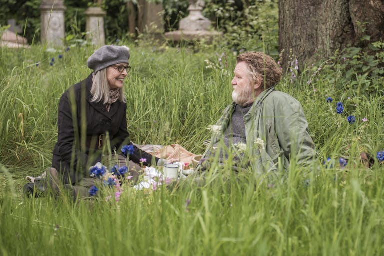 An older man and woman sit in a grassy meadow