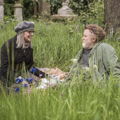 An older man and woman sit in a grassy meadow
