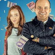 Two men and a woman with red hair smile while bank notes fall around them