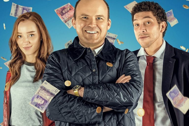 Two men and a woman with red hair smile while bank notes fall around them