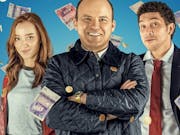 Two men and a woman with red hair smile while bank notes fall around them