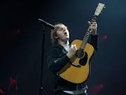 A young white man performs with energetic emotion on stage playing a guitar