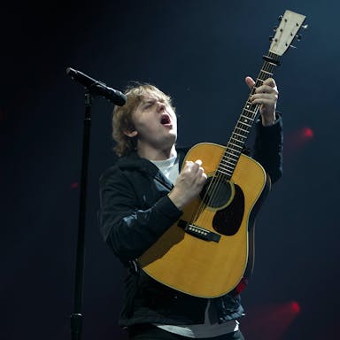 A young white man performs with energetic emotion on stage playing a guitar