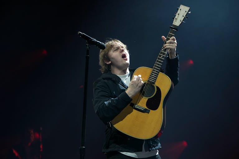 A young white man performs with energetic emotion on stage playing a guitar