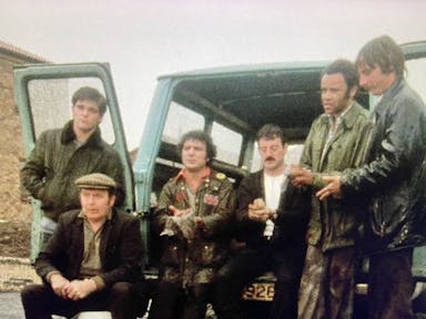 A grainy still of a group of men sitting out the back of a van with its doors open