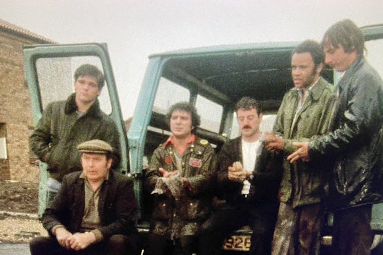 A grainy still of a group of men sitting out the back of a van with its doors open