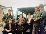 A grainy still of a group of men sitting out the back of a van with its doors open