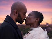 A young black woman and man kiss in front of a sunset view of the London sky.