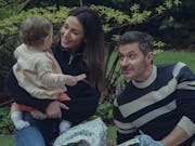 A white woman and white man sitting on the grass playing with a young baby and smiling