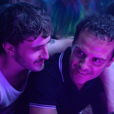 A young white man with his arm around a middle aged white man in a club setting with fluorescent purple light on them 
