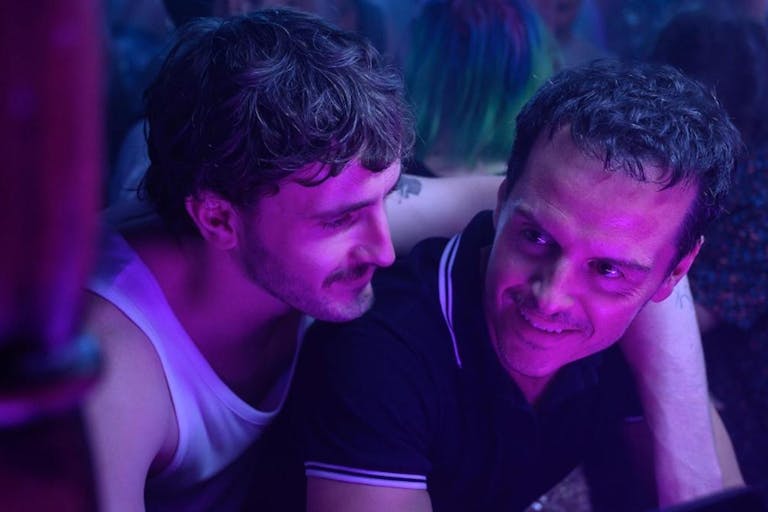A young white man with his arm around a middle aged white man in a club setting with fluorescent purple light on them