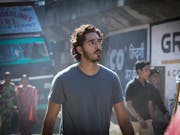 A young Indian man with small beard and wavy short hair walking on a street in India with bustle around him