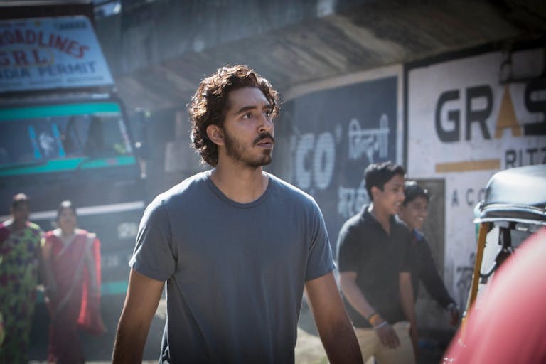 A young Indian man with small beard and wavy short hair walking on a street in India with bustle around him