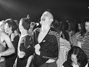 Black and white image of a group of young people looking ecstatic at a rave party.