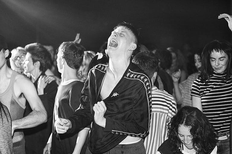 Black and white image of a group of young people looking ecstatic at a rave party. 