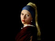A pale young girl with a yellow headscarf and thick blue head wrap wearing a pearl earring, looking over her shoulder at the audience