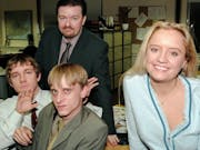 Three white men looking grumpy and one white woman smiling in dated office attire in a boring office setting