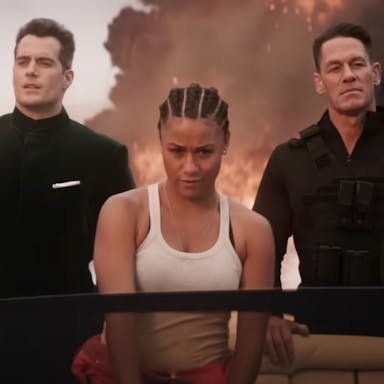 A Black woman in a white vest top and two white men in black suit and black combat clothes riding in a speed boat