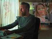 A white man sits at his computer with projected images of white woman around him