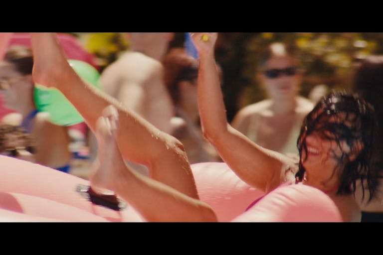 A white woman thrown into a pool with bright pink floats and wet hair over her face smiling
