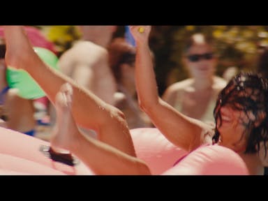 A white woman thrown into a pool with bright pink floats and wet hair over her face smiling