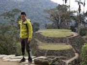 An American Chinese man with a prosthetic leg standing in a epic green landscape and stone built up platforms with paths on Inca Island