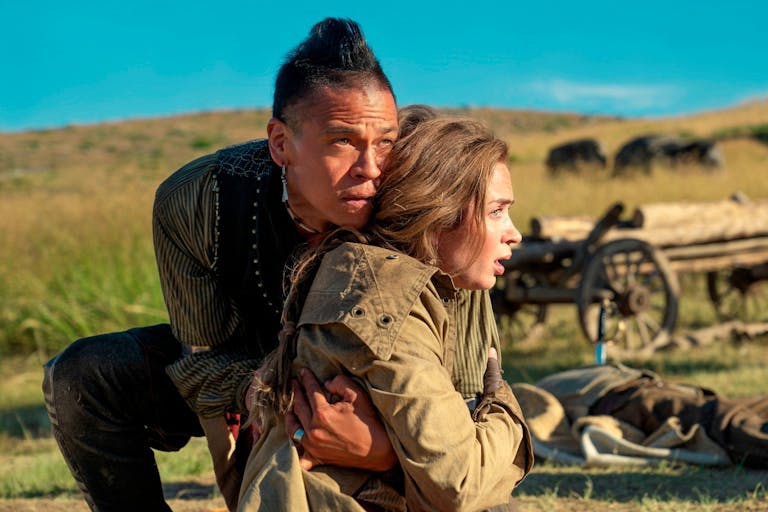 Man holds woman in an embrace  against backdrop of green fields with an old-fashioned wooden cart