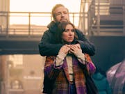 A white couple in autumnal clothing standing in soft outdoor light, embracing